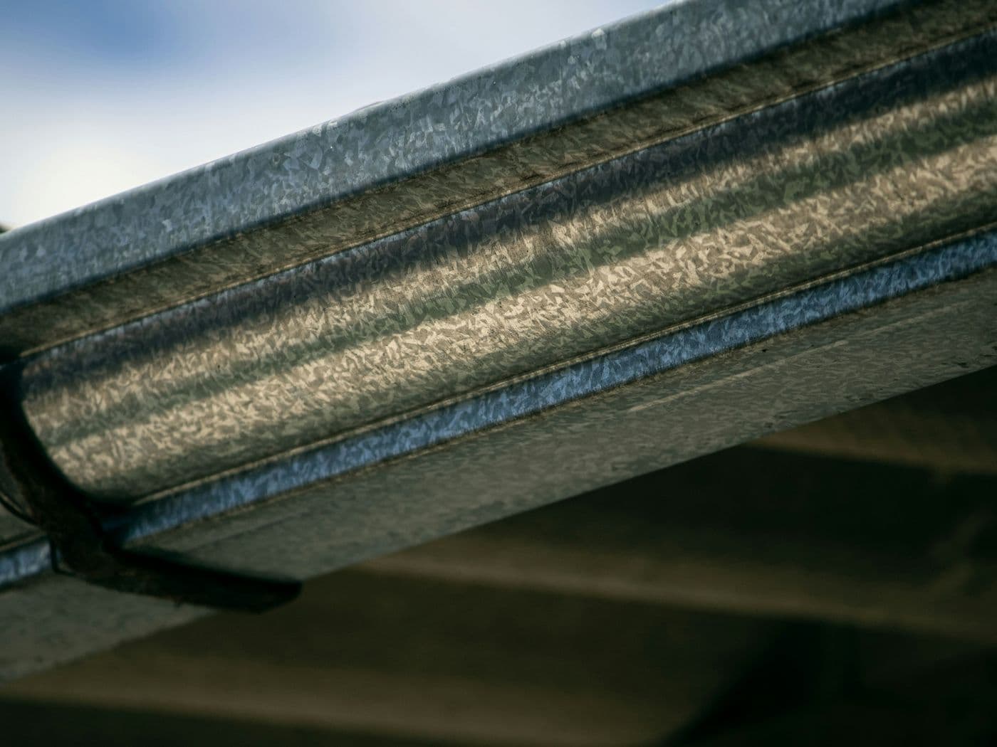Backlit close-up along a galvanized metal gutter running under a roof edge
