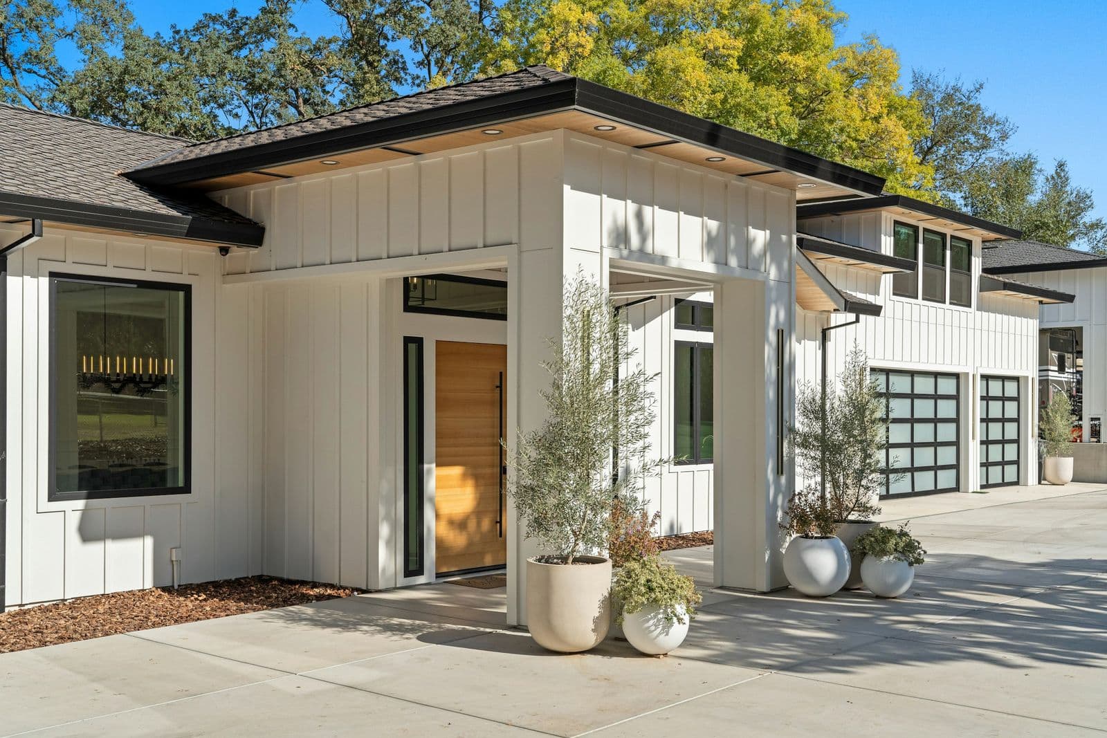 White board-and-batten home with black window trim, a timber front door and glazed garage doors, under a clear sky