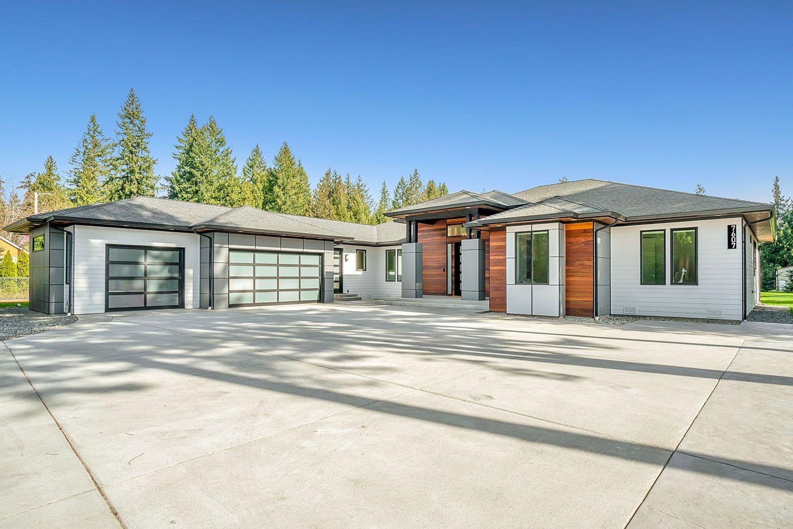 Single-storey home clad in white horizontal lap siding with vertical cedar accent panels, backed by tall evergreens