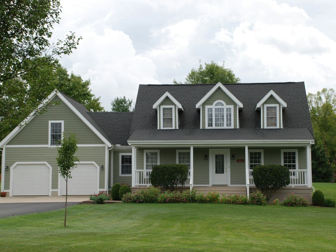 Two-storey home in sage-green horizontal lap siding with white trim, three dormers and a covered porch