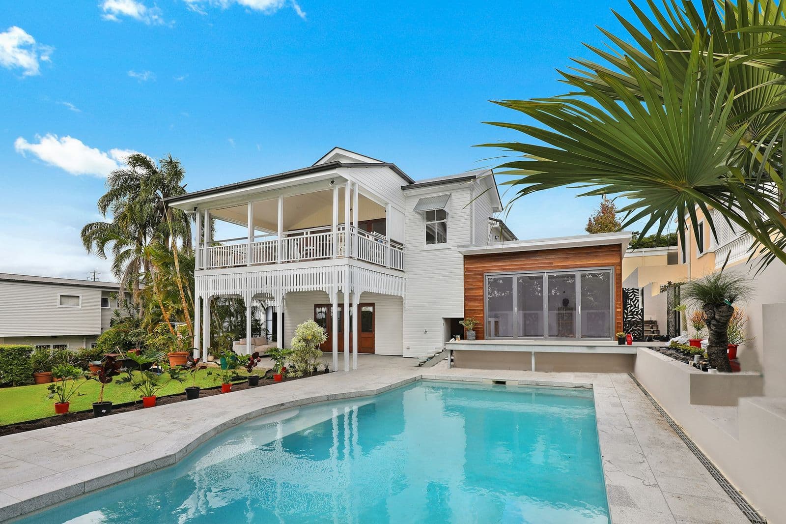White weatherboard home with a covered upper balcony and a timber-clad extension, seen across a swimming pool