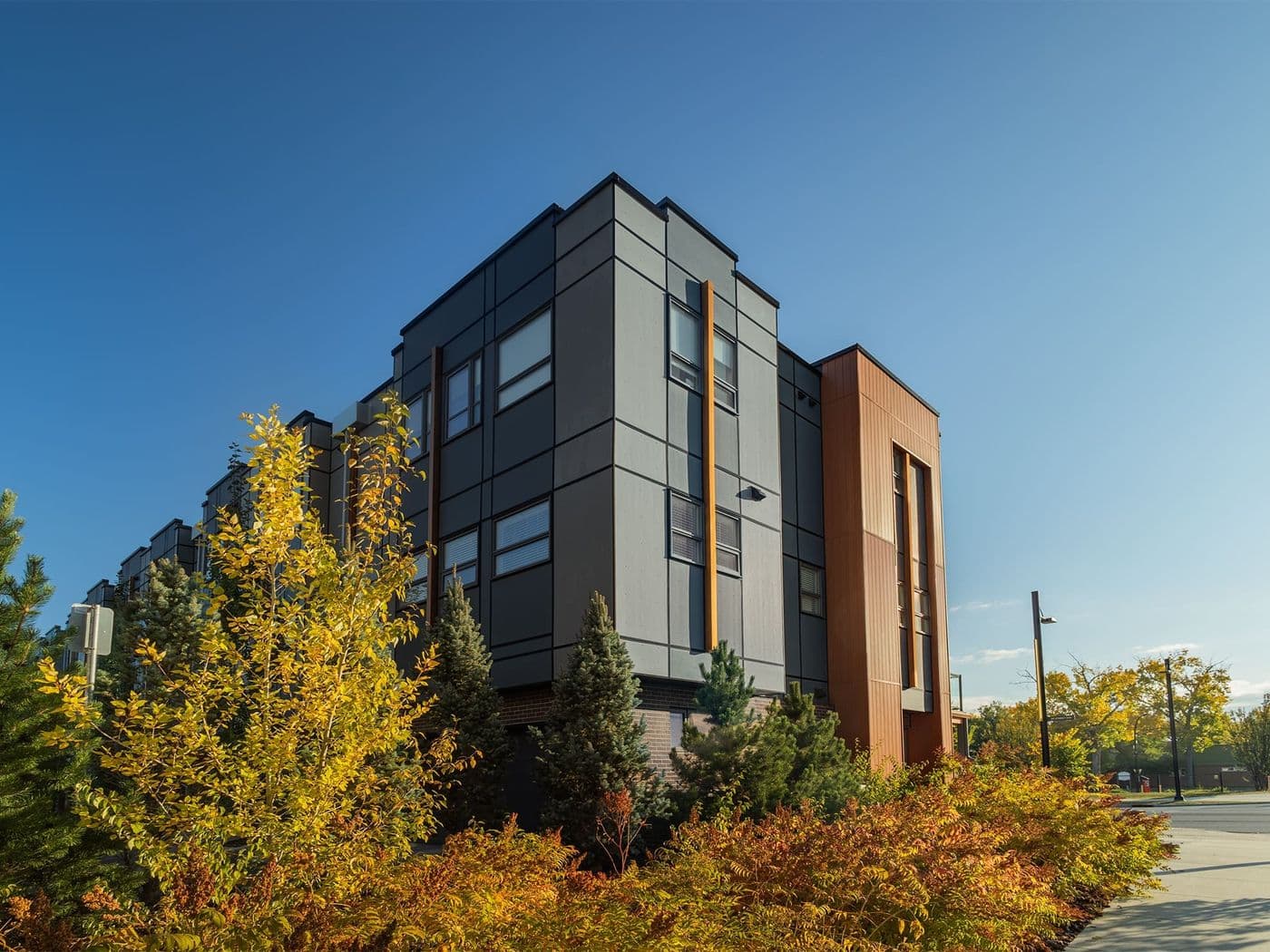 Modern grey townhome corner with a wood-toned vertical panel accent and visible aluminum trim reveal lines.