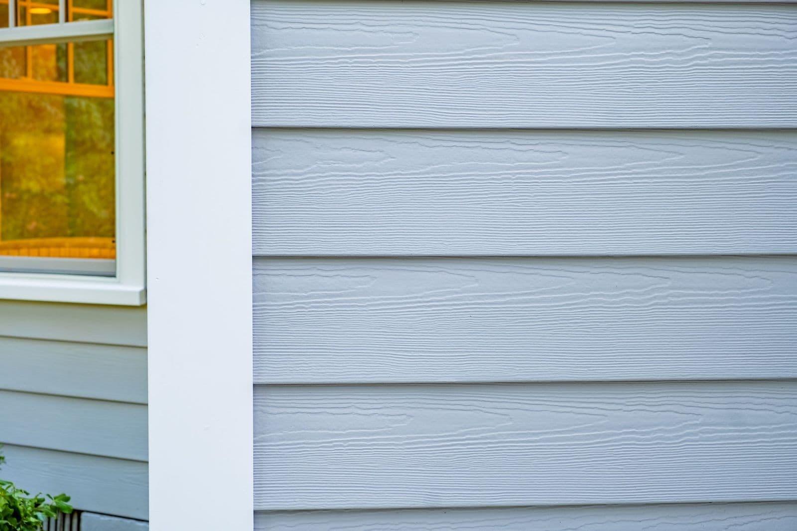 Close-up of grey horizontal lap siding boards showing a cedarmill woodgrain texture, beside a white window trim.