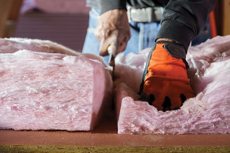 Installer cutting a pink PINK Next Gen Fiberglas insulation batt cleanly with a utility knife.