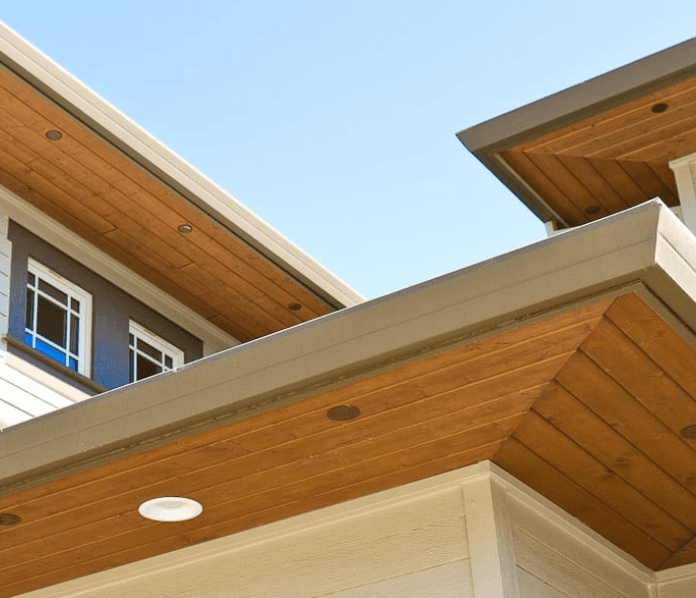 Two rooflines of a modern home finished with stained pine tongue-and-groove soffit boards and recessed pot lights.