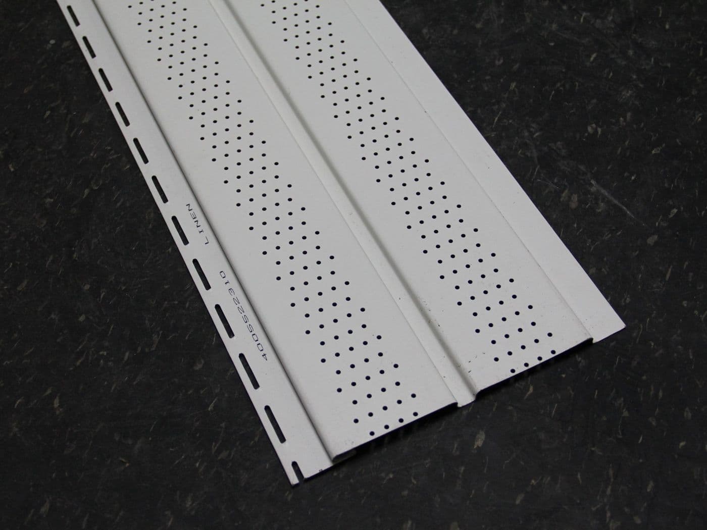 Close-up of a single white vented vinyl soffit panel on a dark stone surface, showing rows of perforated vent holes and a stamped "Linen" colour name near the nailing hem.