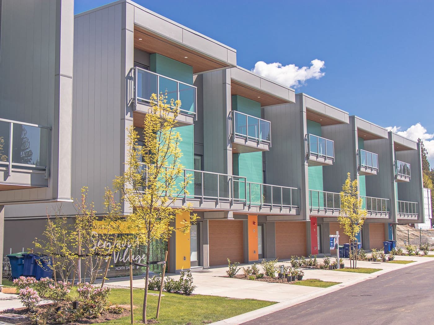 Row of modern grey townhomes clad in vertical HF panel siding, with teal accent panels on the balconies.