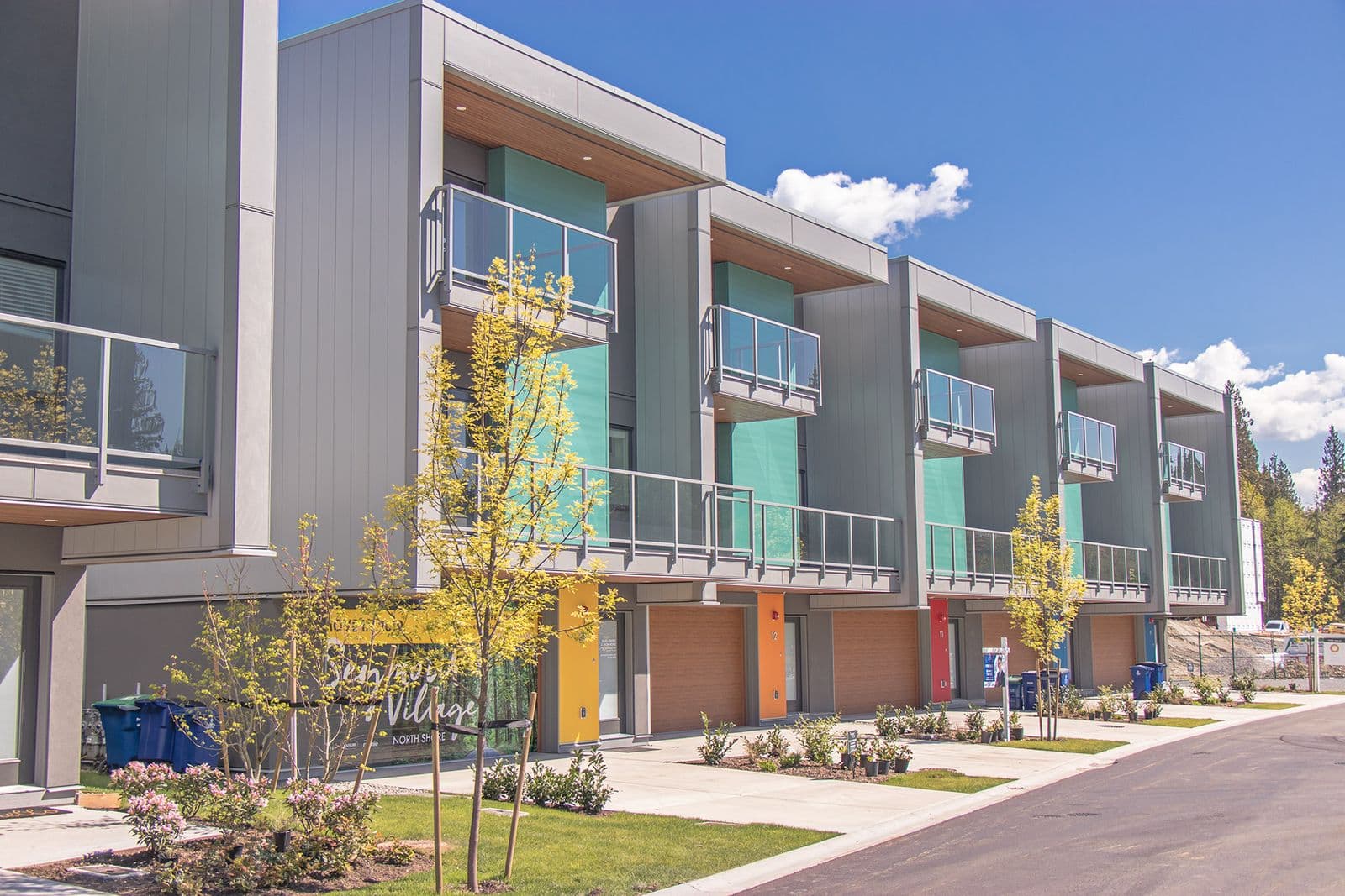 Row of modern grey townhomes clad in vertical HF panel siding, with teal accent panels on the balconies.