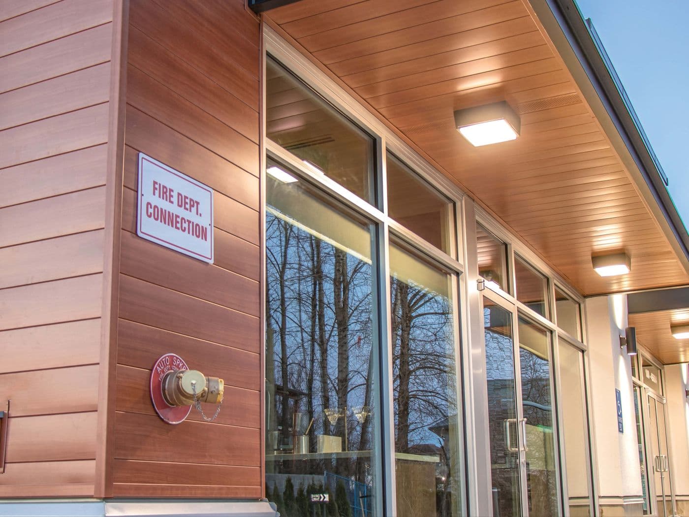 Commercial building corner clad in copper-toned ProBoard metal siding, with a covered walkway and glass storefront windows.