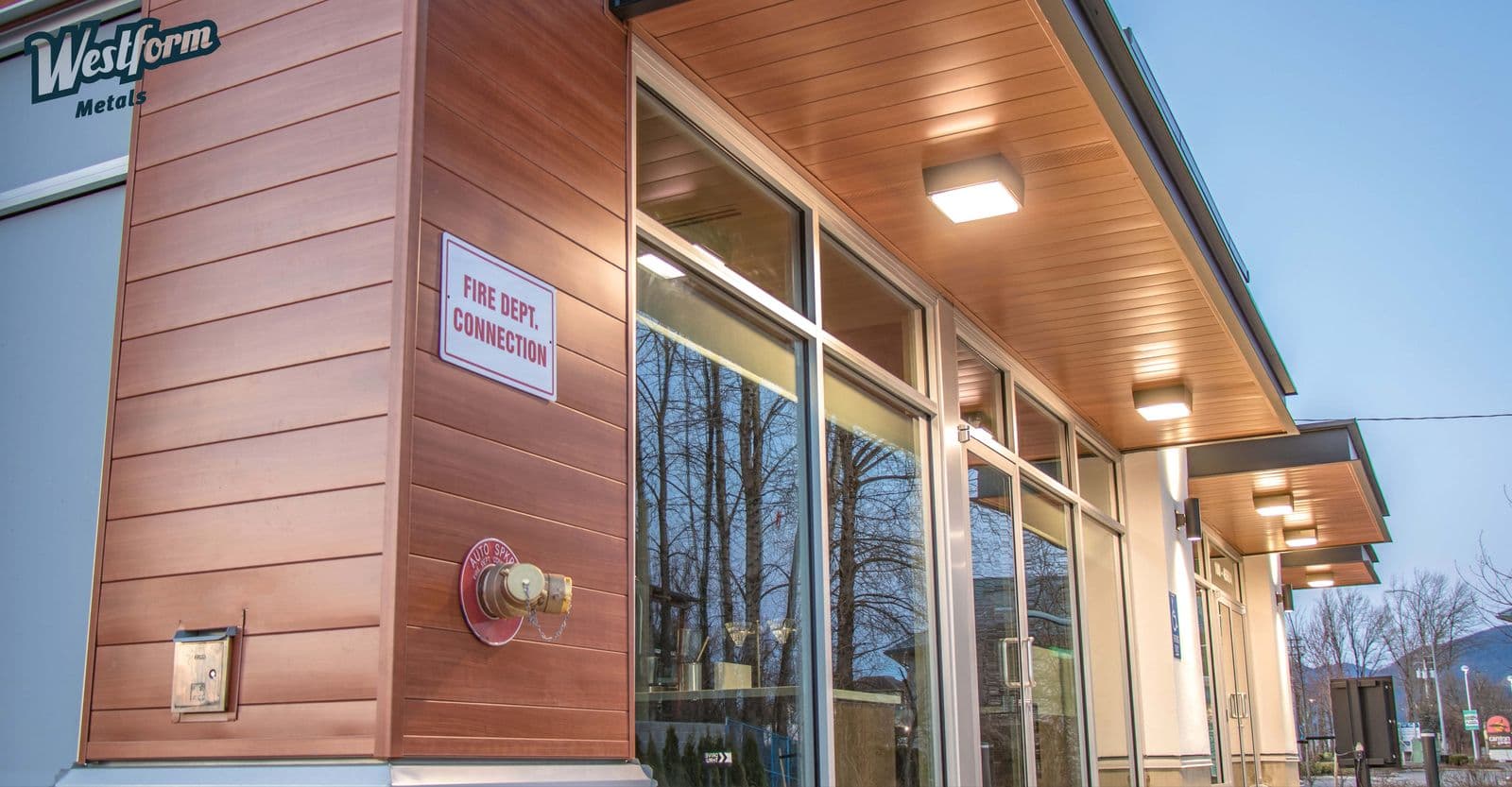 Commercial building corner clad in copper-toned ProBoard metal siding, with a covered walkway and glass storefront windows.